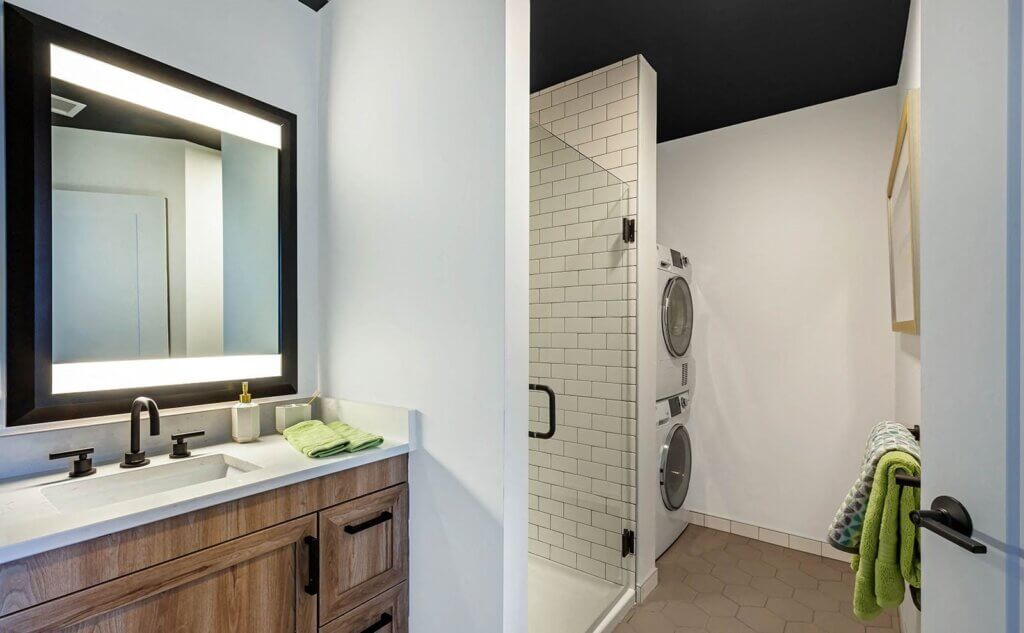bathroom with white walls, off-white tiled shower with glass door, vanity with black framed mirror