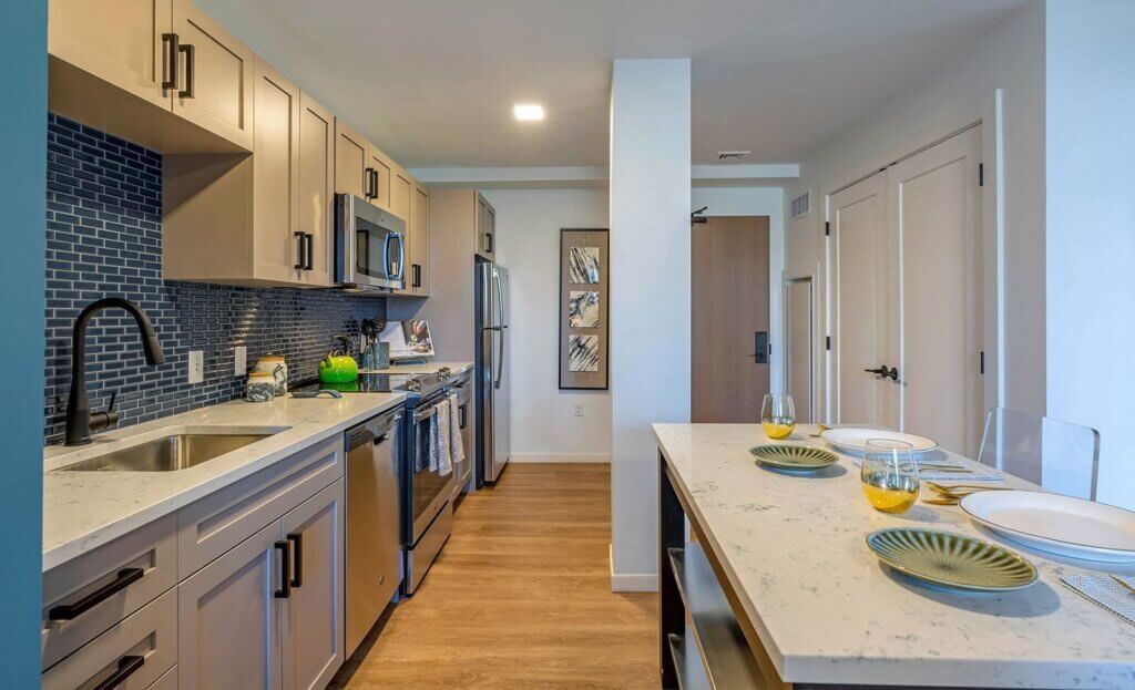 The Brynx one bedroom apartment kitchen with island eating area, marble countertops and cabinets with modern matte black hardware, stainless steel appliances