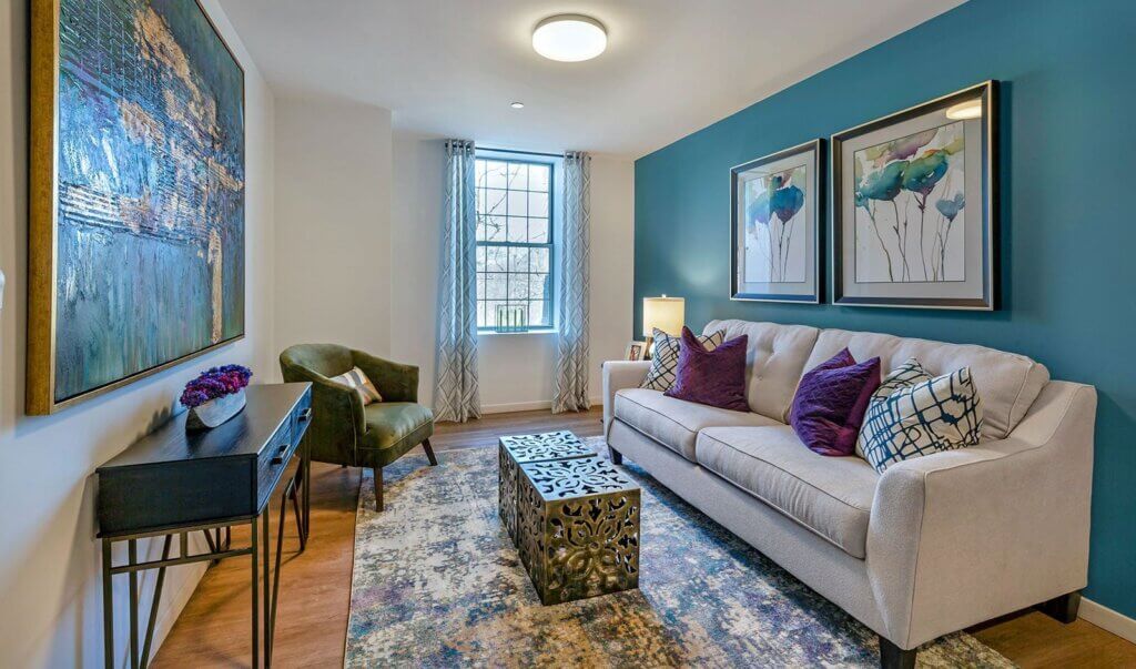 living area with beige couch, blue accent wall, three framed paintings on the walls and arm chair