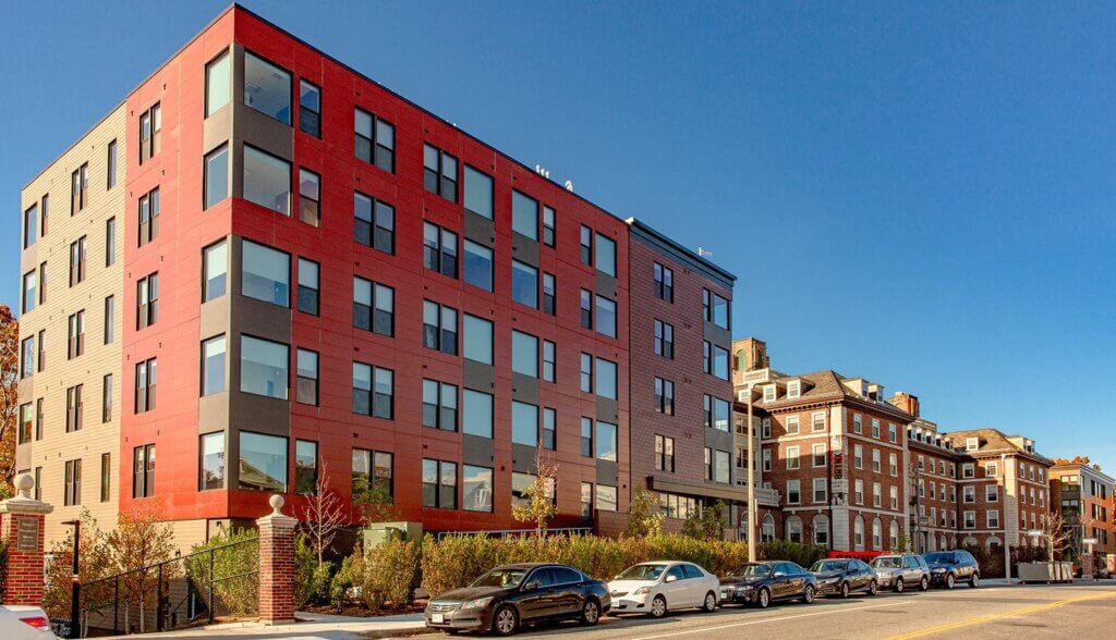 View of The Brynx building during the day from the street. Cars parked along the street in front of the building