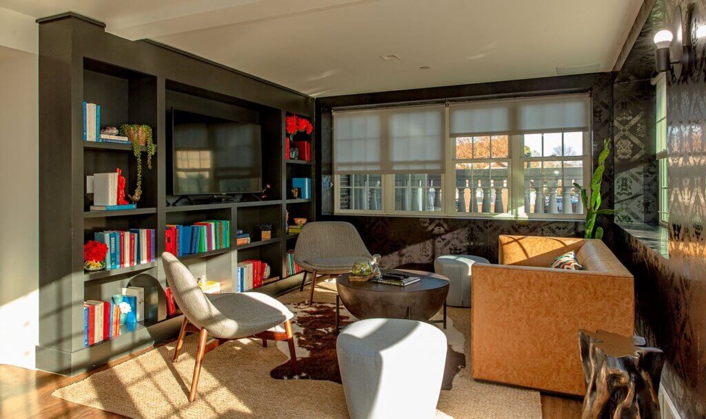 Lounge area of The Brynx with bookshelves and a tv, seating including a couch and multiple chairs, area rug and plants